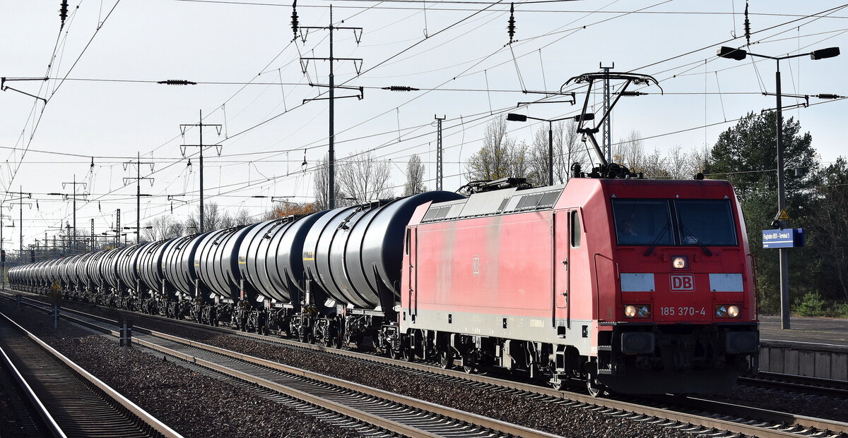 DB Cargo AG, Mainz mit ihrer  185 370-4  (NVR:  91 80 6185 370-4 D-DB ) und einem Kesselwagenzug Richtung Stendell (Schwedt) am 22.11.23 Höhe Bahnhof Flughafen BER Terminal 5.