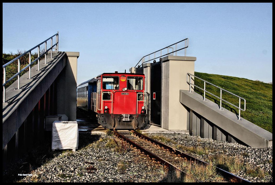 DB Schöma Lok 399108 fährt hier am 1.10.2017 mit einem Personenzug vom Hafen Wangerooge kommend durch das Deichtor in Richtung Bahnhof.