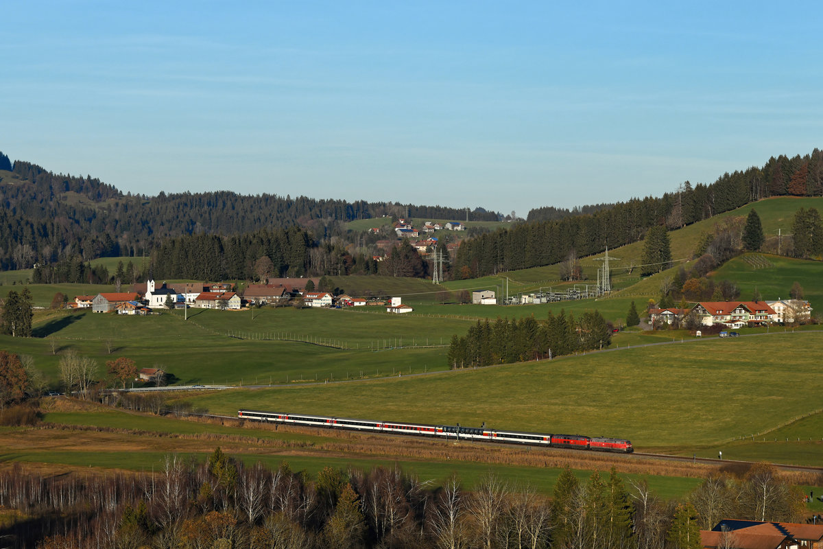 Der anstehende Abschied von den Diesellok-bespannten ECs auf der Allgäubahn zog naturgemäß viele Fotografen von nah und fern an die Strecke. Pandemiebedingt versuchte ich jedoch Massenaufläufe zu vermeiden und suchte bewußt nach eher abgeschiedenen Plätzen. Oberhalb von Oberstaufen hat man einen guten Blick auf die Ortschaft Zell. Von dort aus fotografierte ich am 14. November 2020 allein und ungestört den EC 195 auf seiner Fahrt nach München HBF. Es führten die Mühldorfer 218 423 und 401. 