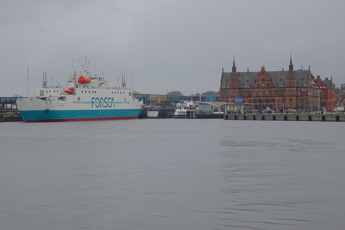 Der Bahnhof von Helsingör liegt direkt am Meer. Züge werden heute nicht mehr trajektiert, aber der Lkw-Verkehr ist erheblich, auch von Fuß-Passagieren wird die Verbindung genutzt. Im Hafen liegt die Fähre  Mercandia IV  der Rederei  Forsea . Die Überfahrt dauert 20 Minuten, alle 20 Minuten fährt ein Schiff. 27. August 2021
