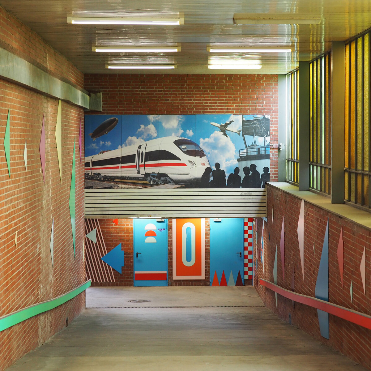 Der Bahnhof Schönefeld aka Flughafen BER – Terminal 5. 
Blick entlang der Rampe vom Empfangsgebäude in den Quertunnel. 
Interessant dabei die Abbildung des Zeppelins, die meines Wissens nach nie in Schönefeld landeten.

Berlin, der 06.08.2021