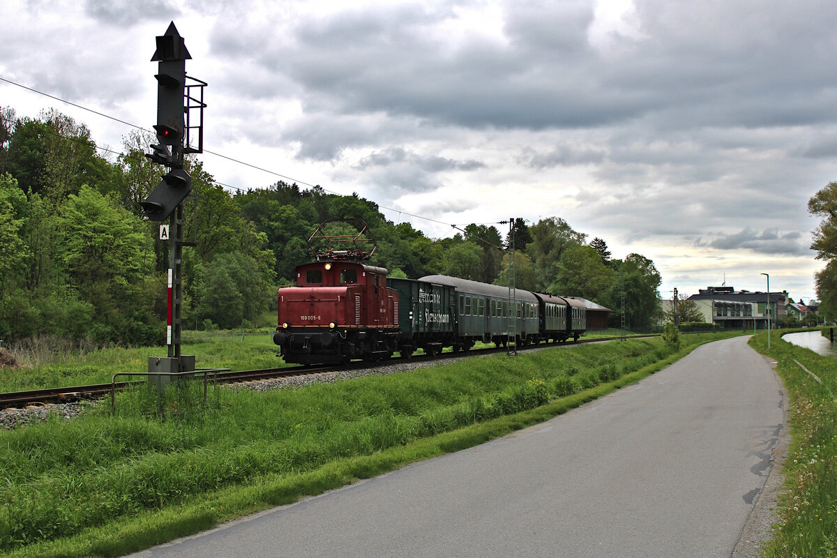 Der Bayerische Localbahn Verein ist mit E69 005 und einem Sonderzug unterwegs zurück von Prien am Chiemsee nach München Ost und verlässt hier gerade bei schwierigen Lichtverhältnissen den Bahnhof Bruckmühl. (18.05.2023)