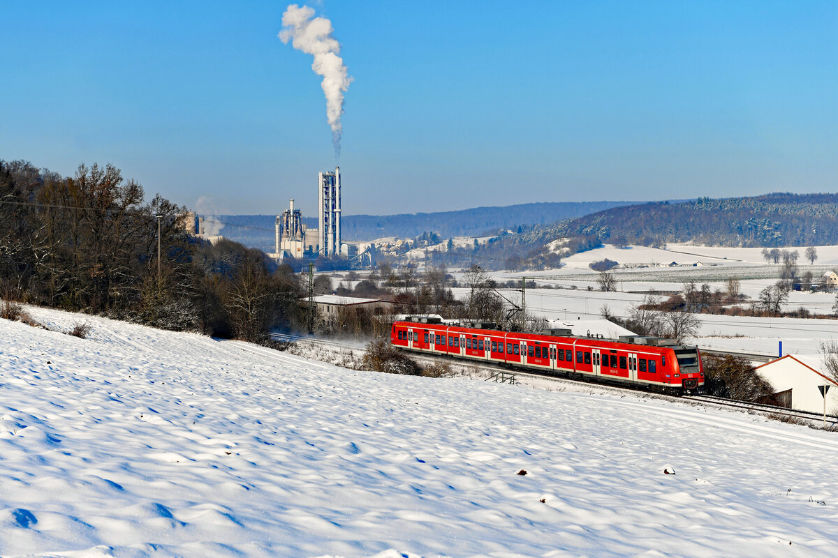 Der Betreiberwechsel von DB Regio auf Go-Ahead Bayern auf der Riesbahn von Aalen über Nördlingen nach Donauwörth zum Fahrplanwechsel am 11. Dezember 2022 verlief mehr als holprig. Aufgrund von Personalmangel war es nicht möglich, den Betrieb mit eigenen Fahrzeugen zu starten. Durch intensive Bemühungen gelang es Go-Ahead Bayern zumindest, die Firmen DB Regio und Weser Ems Eisenbahn GmbH (WEE) mit einem Ersatzzug-Konzept zu beauftragen, um den Zugverkehr sicher zu stellen. Die Deutsche Bahn setzte dabei einen Triebzug der Baureihe 425 ein. Während der Start beim anderen einspringenden Unternehmen ebenfalls suboptimal lief, fuhr DB Regio von Anfang an zuverlässig. Am 17. Dezember 2022 zeigte sich das Donau-Ries verschneit bei besten Wetterbedingungen. Bei Ebermergen konnte ich den 425 545 auf seiner Fahrt als RB 57671 von Aalen nach Donauwörth fotografieren. Im Hintergrund erkennt man das eindrucksvolle Zementwerk bei Harburg. 