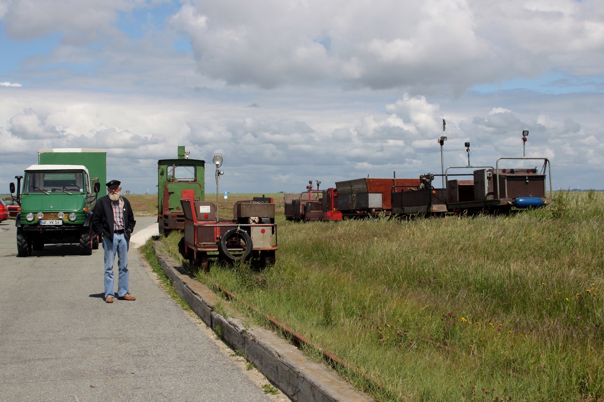 Der Bf auf Hallig Langeness am 14.06.2012 mit 6 abg. Privatloren und der Lok 2 des LKN-SH. Links wartet der  Langeness Express  (siehe auch Bild 912675) auf eine Gruppe angehender Bauingeneure, die wenig später mit dem Sambawagen kommen werden.