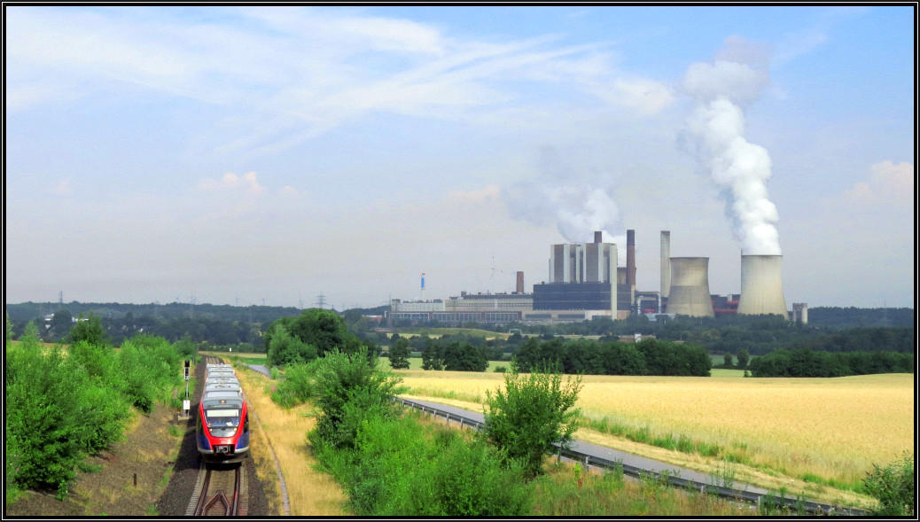 Der Blick auf das Braunkohlekraftwerk Weisweiler der RWE. Hier wird der Strom für die gesamte Region Aachen - Düren erzeugt. Ohne Strom dagegen kommt der Talent links im Bild aus,dieselelektrisch angetrieben ist er gerade als RB20 unterwegs nach Langerwehe. Landschaftsszenario vom 05.Juli 2015.