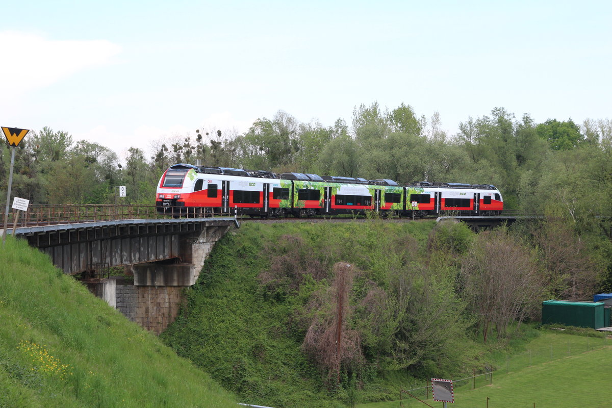 Der Cityjet Eco 4746 049 ist eine Testversion des ÖBB Cityjet für Akkubetrieb. Aufgeladen werden die Akkus, die sich in den Dachaufbauten befinden während der Fahrt unter Fahrleitung, im Stand unter Fahrleitung sowie beim dynamischen Bremsen mit der gewonnenen Energie aus der E-Bremse auch im Akkubetrieb.
Am 28.4.2020 fuhr der 4746 049 als R4177 von Spielfeld-Straß nach Bad Radkersburg und überquert hier kurz hinter Spielfeld-Straß zuerst die Brücke über eine Landesstraße und anschließend die Brücke über die Mur.