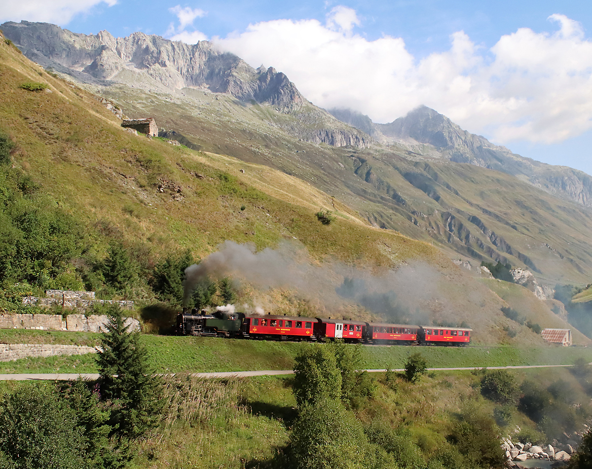 Der Dampfzug von Realp nach Furka - Gletsch - Oberwald erklimmt die 130 Promille-Strecke kurz nach Realp. Das Foto wurde von der anderen Talseite aufgenommen. Realp, 26.8.2023