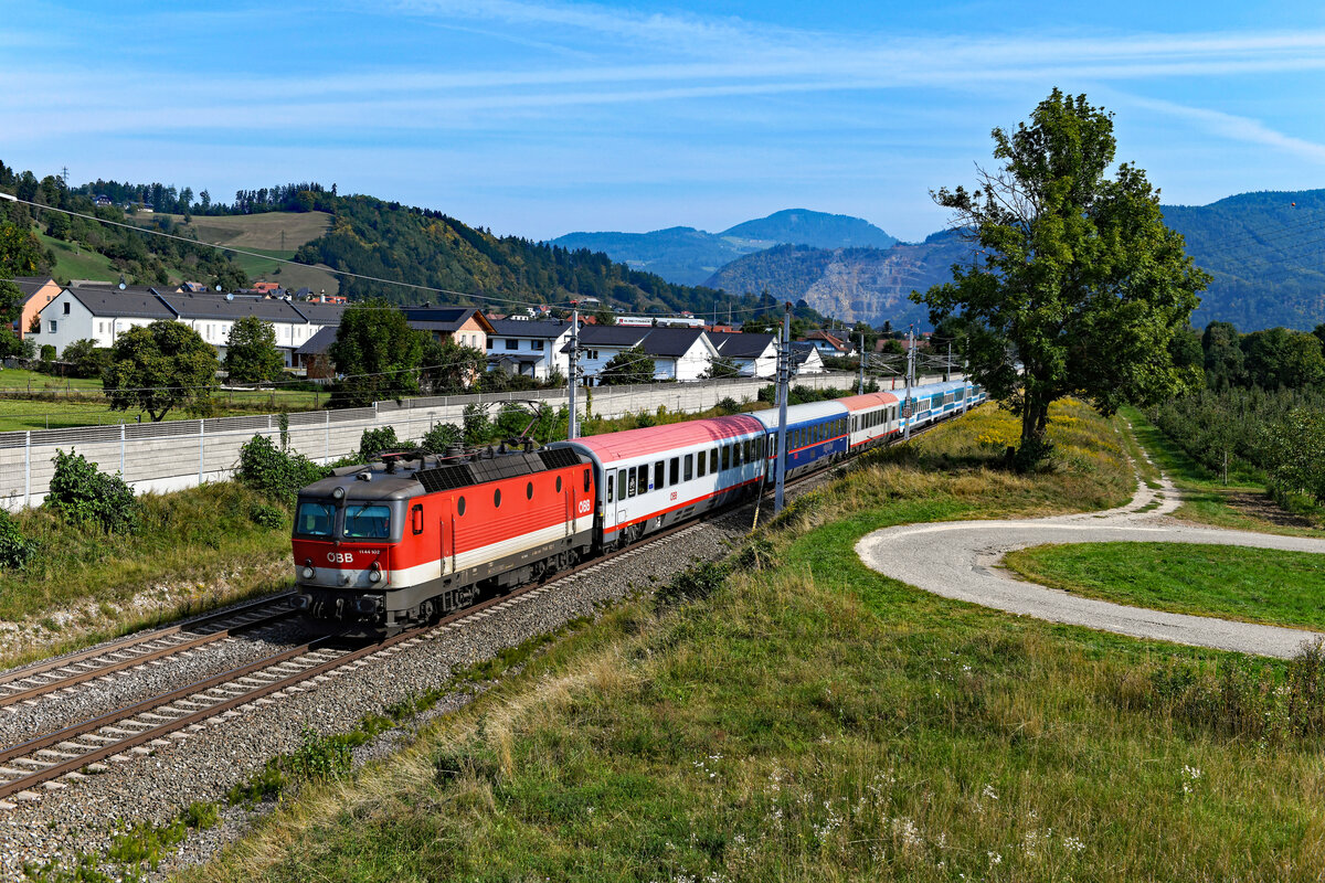 Der EC 151  Emona  von Wien HBF nach Ljubljana ist noch ein klassischer internationaler Fernzug. Bis Ende 2021 war dieser EuroCity eine der wenigen verbliebenen hochwertigen Reisezugleistungen für die Baureihe 1144. Seit Fahrplanwechsel ist der Schnellzug über den gesamten Laufweg hinweg mit einem ELL-Vectron bespannt. Der Lokwechsel an der Grenze kann somit entfallen. Am 14. September 2021 hatte die 1144.102 die Aufgabe, den Zug bis nach Spielfeld-Straß zu befördern. Bei Kleinstübing gelang eine Aufnahme. 