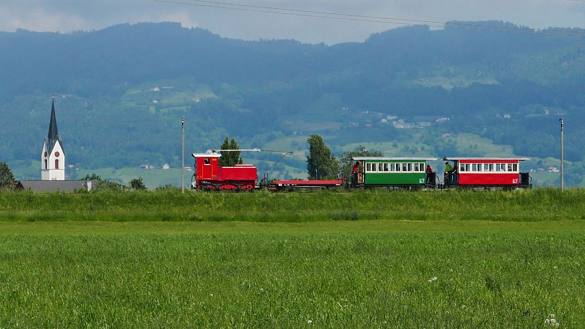 Der von der elektrischen/dieselektrischen Lok  URS  gezogene Zug befindet sich am 30.05.2019 kurz vor dem Streckenunterbruch in Kriessern. Das bedeutet dann für die Fahrgäste dort auszusteigen und zu Fuß vom schweizerischen Kriessern über die Rheinbrücke ins österreichische Mäder zu laufen um dann in den Anschlusszug zum Steinbruch Kadelberg bei Mäder/Koblach einzusteigen.