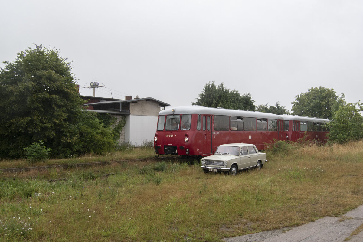 Der Fahrgastverband Pro Bahn unternahm am 12.07.2025 zwecks der Reaktivierung des Personenverkehrs, der Bahn zwischen Neubrandenburg-Friedland, eine Sonderfahrt. Nach 11 Jahren somit der nächste Sonderzug auf der Strecke. Für die ca. 26Km lange Strecke benötigen die Züge 90 Minuten, mit größtenteils nur mit 10-20Km/h gefahren werden. Kein Wunder, das Gleis ist marode und wird zunächst 2025 für 9 Millionen Euro ausgebessert. Das heißt Holzschwellen werden ersetzt und Bahnübergänge erneuert und eine Geschwindigkeit von 70Km/h angestrebt. Der Haltepunkt Neuenkirchen ist sehr verbaut und verwachsen. Durch weitere anwesenden Fotografen war ein andere Perspektive nicht möglich. Der Bahnsteig ist links im Bild noch zu erkennen. Vor dem Sonderzug mit der 172 001 steht ein 1200 Lada mit einem alten Kennzeichen. 