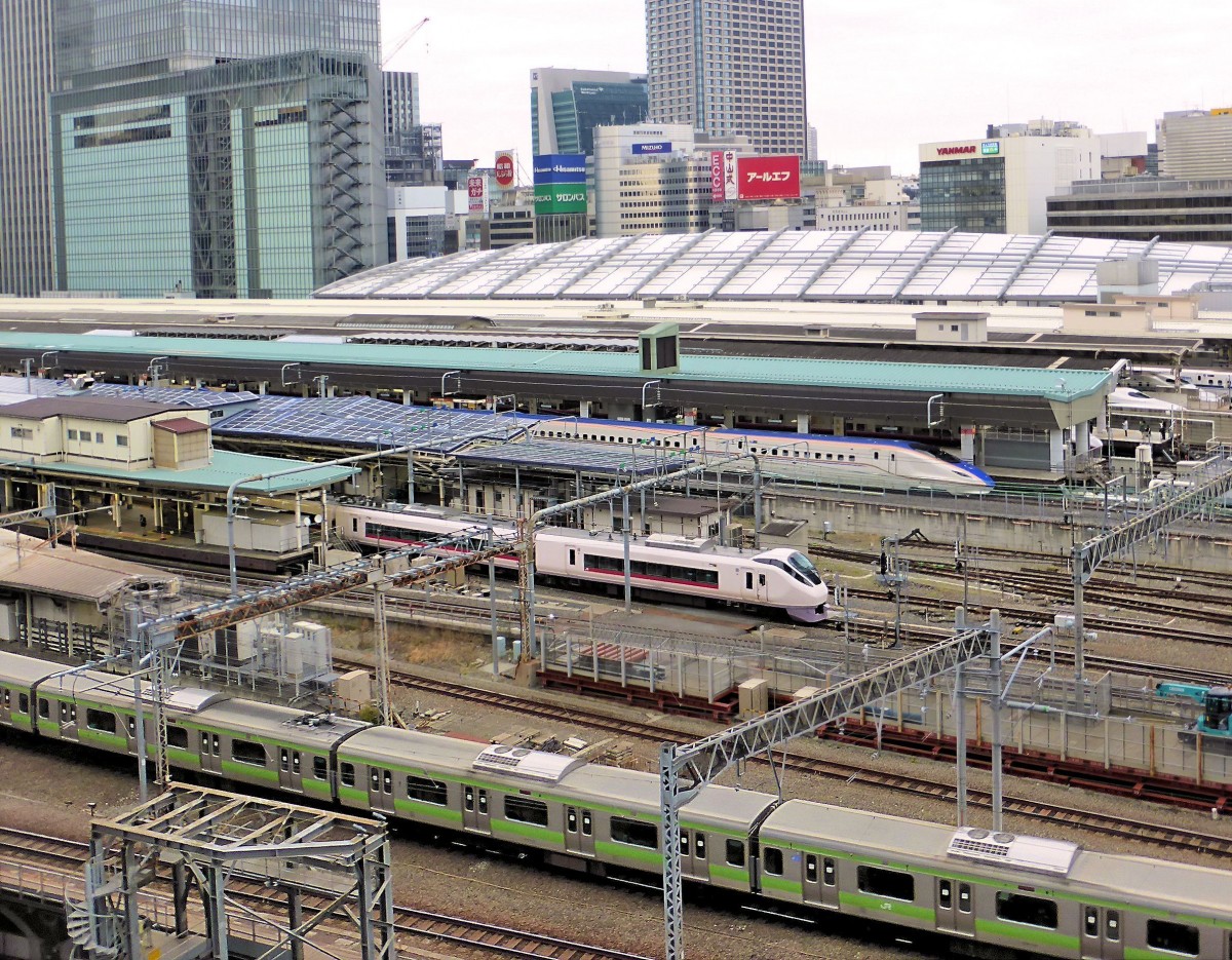 Der Hokuriku-Shinkansen am Tokyo Hauptbahnhof: In der Bildmitte wartet ein Zug Typ E7 / W7 auf Abfahrt nach Kanazawa. Davor fährt ein Intercity (1067mm-Spur) Serie 657 auf der Fahrt nach Mito und Hitachi (an der Küste nordöstlich von Tokyo) ein. Ganz vorn ein S-Bahnzug Serie 231 der grünen Linie (Ringlinie). 9.April 2015.     