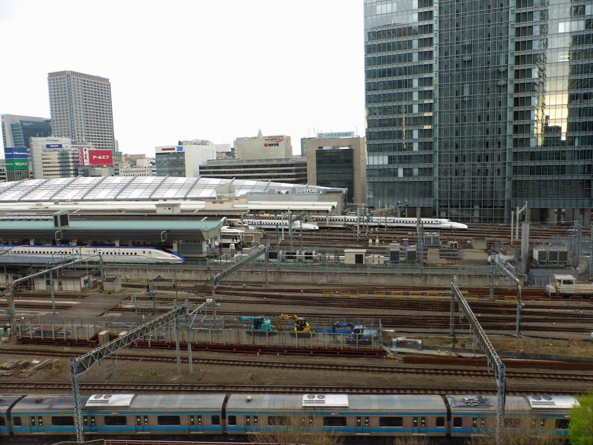 Der Hokuriku-Shinkansen am Tokyo Hauptbahnhof: In der Bildmitte wartet ein Zug des Hokuriku-Shinkansen. Im Hintergrund Shinkansen-Züge (Serie N700) Richtung Kyoto, Osaka und der japanischen Südinsel Kyûshû. Ganz vorn ein S-Bahnzug (Serie 233) der blauen Linie (Nord-Süd-Durchquerung von Tokyo). 9.April 2015. 
