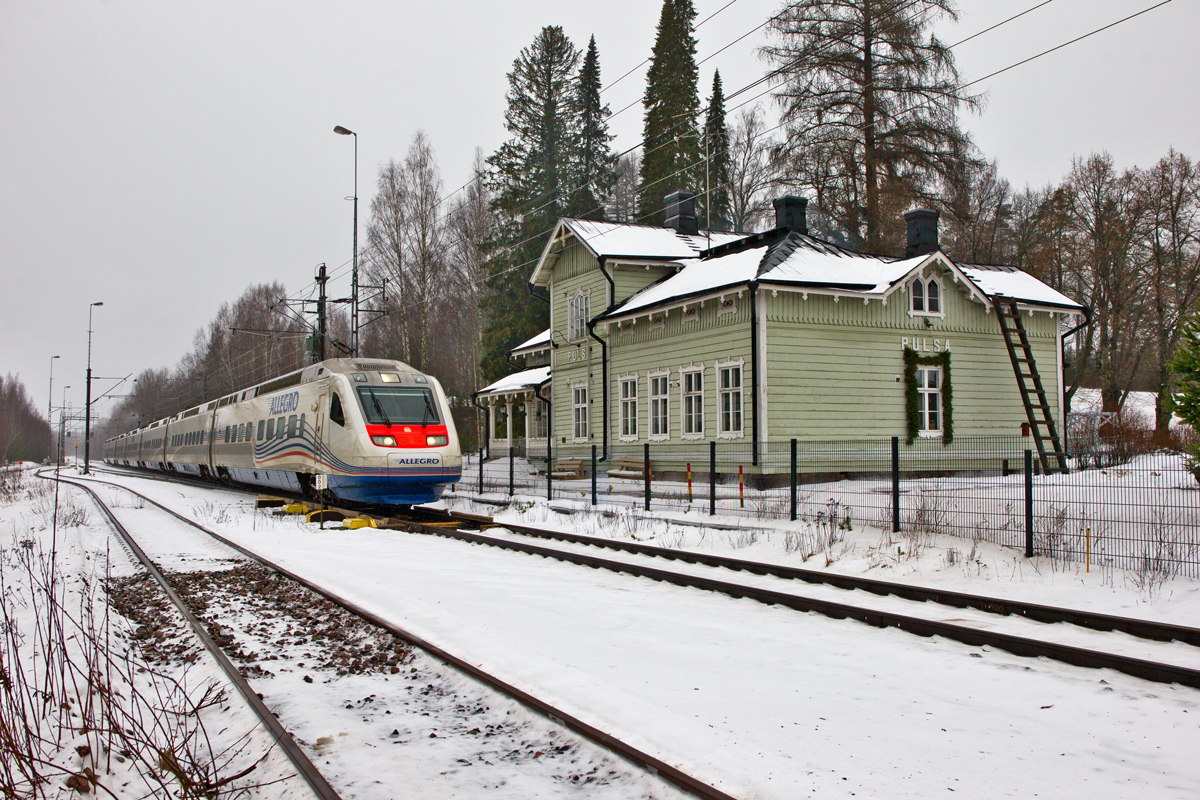 Der  Karelian Train  Allegro braust bei typisch trübem finnischem Wetter am verlassenen Bahnhof Pulsa,kurz vor der finnischen Grenze,aus Helsinki kommend nach St.Petersburg vorüber.Bild vom 28.1.2016