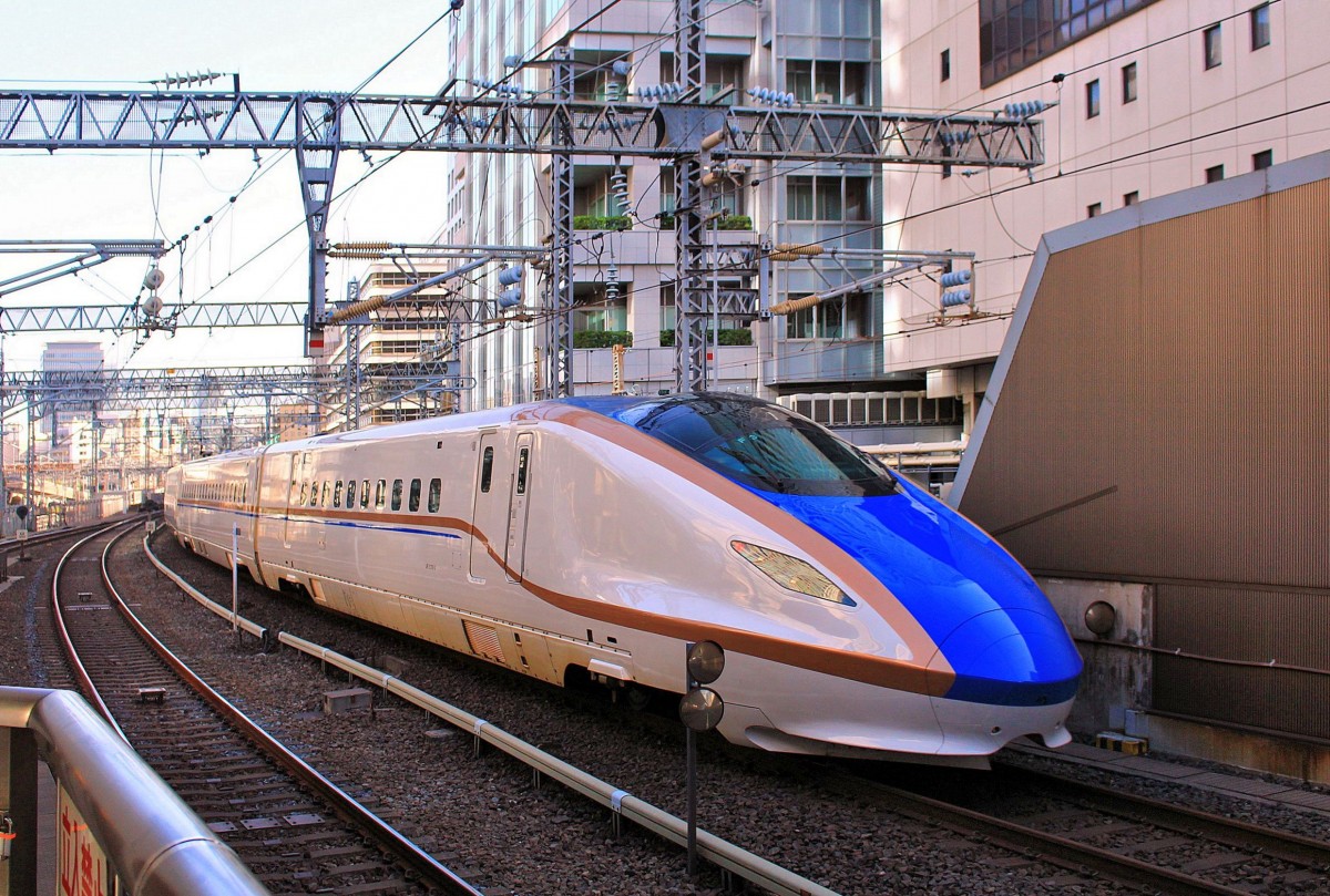 Der Nagano- und Hokuriku-Shinkansen: Die 117,4 km Hochgeschwindigkeitsstrecke (1435mm-Spur) von Takasaki nordwestlich von Tokyo bis in die Gebirgsstadt Nagano wurde am 1.Oktober 1997, rechtzeitig für die Olympischen Spiele in Nagano (7.-22.Feb.1998), eröffnet. Die Fortsetzung dieser Strecke ans Japanische Meer und von da nach Westen zu den grossen Städten Toyama und Kanazawa ins sogenannte Hokuriku-Gebiet ist nun am 14.März 2015 dem Betrieb übergeben worden. Jetzt heisst die gesamte Strecke Hokuriku-Shinkansen (345,5 km Takasaki-Kanazawa, dazu Mitbenützung einer älteren Linie Tokyo-Takasaki 105,0 km, sowie ca. 10 km Dienstgleise zu den Unterhaltsanlagen westlich von Kanazawa). Die Reisedauer Tokyo-Kanazawa beträgt rund 2 Std. 30 Min (gegenüber 6 Std. 20 Min. im Jahre 1973). Takasaki-Nagano liegt zu 51 % in Tunnels, Nagano-Kanazawa zu 44 %. Wechselstrom 25 000 V/teils 50, teils 60 Hz. Im Bild Ausfahrt eines neuen E7/W7-Zuges (E723-1) aus dem Hauptbahnhof Tokyo mit Ziel Nagano, 27.September 2014. Für den Hokuriku-Shinkansen wurden 27 Züge zu 12 Wagen (für 260 km/h) 2013/14 beschafft. 17 Züge E7 gehören JR-Ostjapan, 10 Züge W7 gehören JR-Westjapan. 