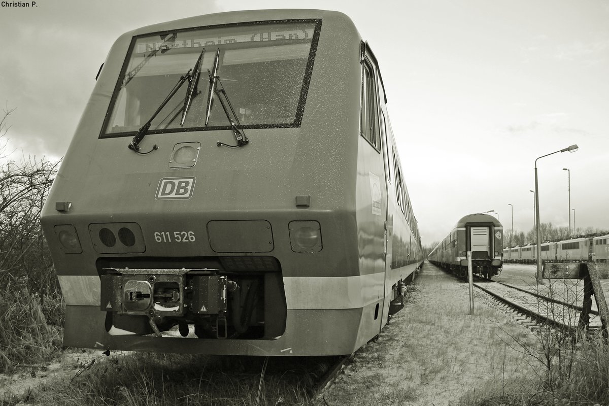 Der Pannolino (dt. Windel), abgeleitet aus dem Vorgängermodell VT 610  Pendolino , hatte als rein  Deutsches  Fabrikat seine Schwierigkeiten sich gegenüber dem  Italiener  zu behaupten, da er mit im Militär verwendeter Technik ausgestattet war, die damals wie heute sehr Fehler belastet ist.
Der 95 80 0611 026-5 D-DB/95 80 0611 526-4 D-DB ist einer von nur rund fünfzig VT 611 (Verbrennungstriebwagen mit Neigetechnik) die gebaut wurden, bis der Großauftrag der Bundesbahn storniert wurde. Seit dem 15.12.15 ist nun das Stillstandsmanagement der DB die letzte Heimat der Neigetechnik Flotte.
Die zuletzt im Bw Ulm bei der DB ZugBus Regionalverkehr Alb-Bodensee GmbH beheimateten 16 Triebzüge der Baureihe 611.0 die im SSM Mukran stehen, haben in den Zug Ziel Anzeigen (ZZA) Northeim (Han) und Itzehoe stehen.
leider wird ein Teil der Triebwagen von Mukran aus nurnoch eine Reise antreten, wenn sie nicht vor Ort zerlegt werden.
Auffällig ist, das Verbrennungstriebwagen mit Neigetechnik bei der DB keine große Karriere zu erwarten haben.
Der 611 als zeite Neigetechnik Baureihe der Bundesbahn hat noch gut 21 Jahre sich behaupten können.
Die VT 612 werden in absehbarer zeit das Selbe schiksahl erleiden, und die ICE TD (Baureihe 605) hat nach Verhältnismäßig kurzer Betriebszeit ein Kaotisches Ende (bei der DB) ereilt.
Hoffentlich werden die verbleibenden  Muhikaner  noch eine Weile fahren.


(Kein Gleisbereich, vom Gehweg aus Fotografiert)