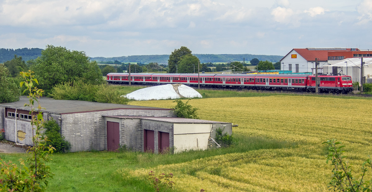 Der RE nach Stuttgart hatte am 24.6.13 gerade in Schnelldorf gehalten und fuhr zwischen alten und modernen Industriegebäuden hindurch westwärts.