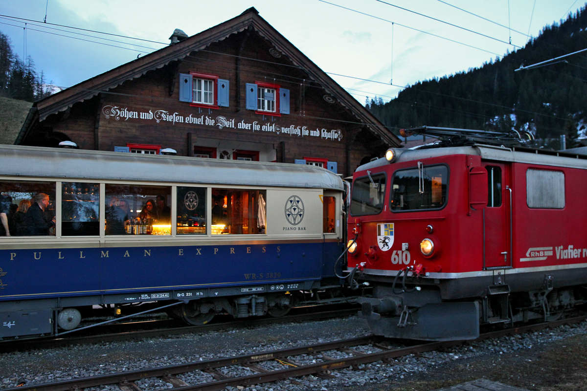 Der Rhb Nostalgiewagen Alpine Pullman Express/Pianobarwagen bei einem kurzen Halt vor dem Bahnhofsgebäude Langwies,daneben die wartende Ge 4/4 I 610.Bild vom 13.12.2014