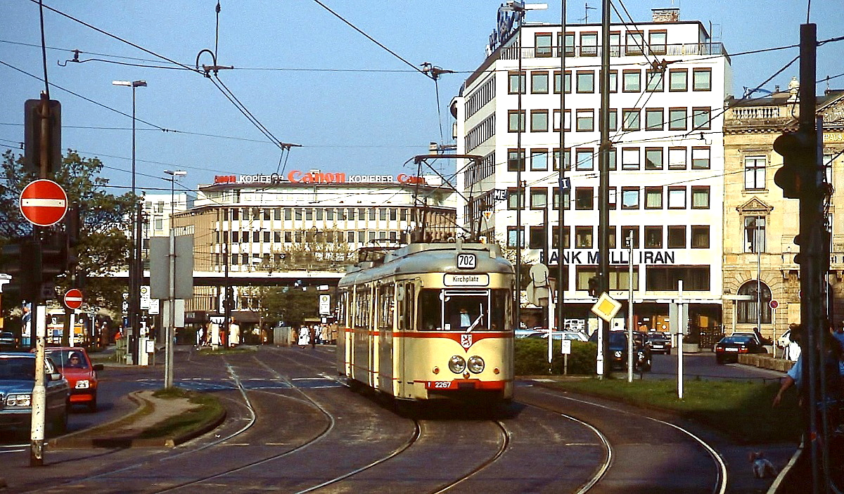 Der Rheinbahn-Tw 2267 verlässt um 1990 die Haltestelle Jan-Wellem-Platz. Diese Zweirichtungsfahrzeuge vom Typ K66 wurden 1966 für die Fernbahnlinie K beschafft, um die dort noch benötigten Triebwagen aus den 1920er Jahren zu ersetzen. Nach der Ablösung durch die in den 1970er Jahren in Dienst gestellten GT8 wurden sie auf innerstädtischen Linien, zuletzt auf der 702, eingesetzt. Vom Jan-Wellem-Platz, dem einstmals größten Straßenbahnknotenpunkt in Düsseldorf mit acht Bahnsteiggleisen, ist nicht viel übrig geblieben. Heute führen noch je zwei Gleise in Nord-Süd- bzw.Ost-West-Richtung. Im Januar 2016, nach Inbetriebnahme der Ost-West-U-Bahn, wird auch der hier abgebildete Streckenabschnitt verschwunden sein.