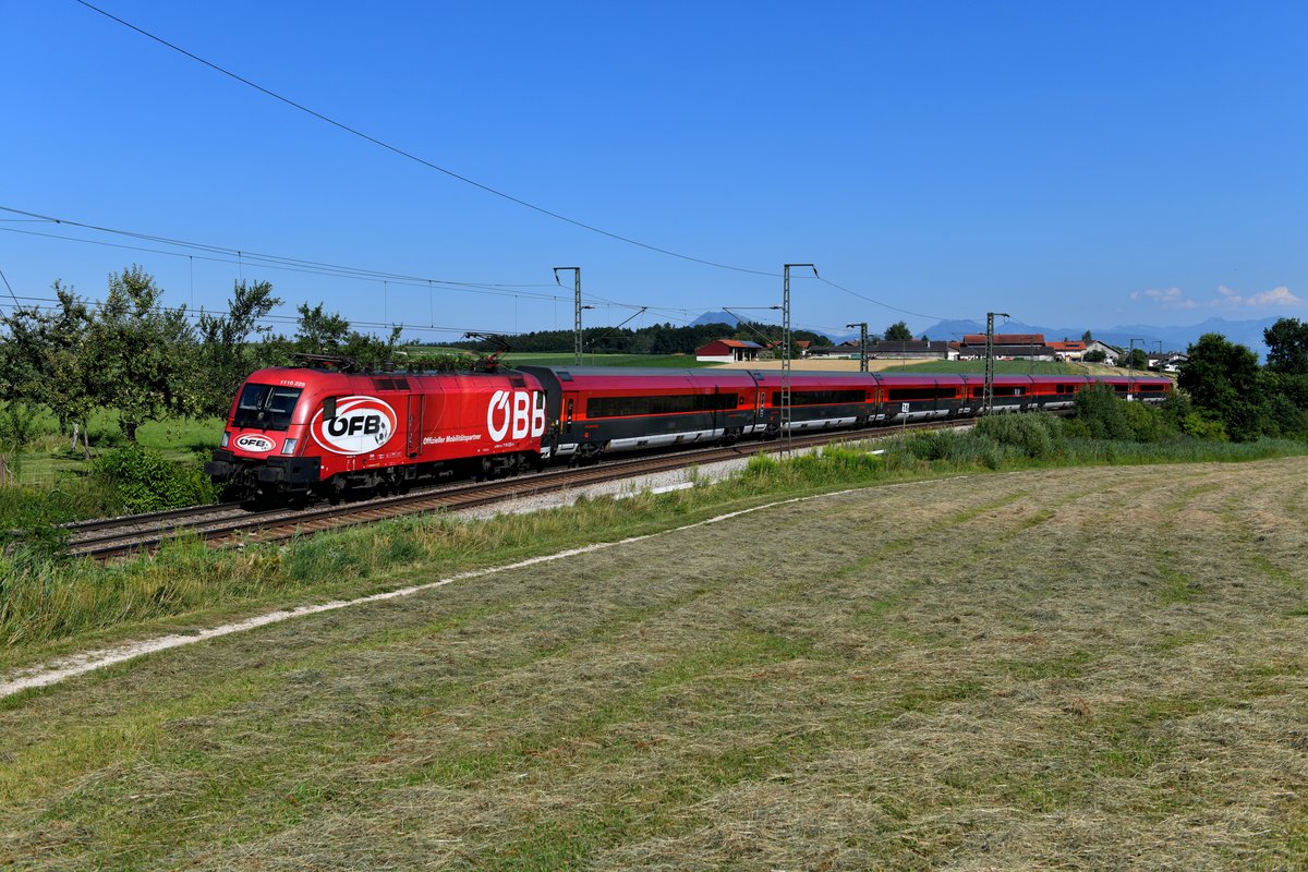 Der RJX 864 vom Flughafen Wien nach Bregenz wurde am 24. Juli 2019 - wie schon am Vortage - von 1116.225 geführt. Die Lok zeigte zum Aufnahmezeitpunkt immer noch die äußere Gestaltung, mit der auf die Kooperation zwischen der ÖBB und dem Österreichischen Fußballbund hingewiesen werden sollte. Die dazugehörige Wagengarnitur hatte bereits seit geraumer Zeit ihre Folien verloren. In flotter Fahrt wird der Korridor durcheilt, nächster Halt ist erst wieder in Wörgl in Tirol. Aufnahmeort war diesmal Amersberg im Berchtesgadener Land. 