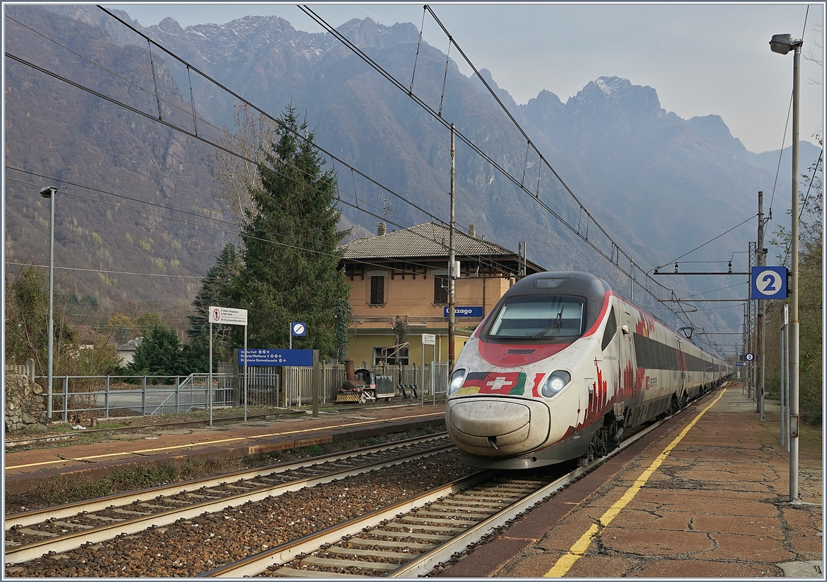 Der SBB RABe 503 022-7  Johann Wolfgang von Goethe  fährt als EC 151 von Milano nach Frankfurt durch den Bahnhof von Cuzzago Richtung Domodossola, welches in gut einer viertel Stunde erreicht wird.
Auf dem Bahnsteig 1 wartet eine kleine Dampflok vergeblich auf die Weiterfahrt.
29. Nov. 2018