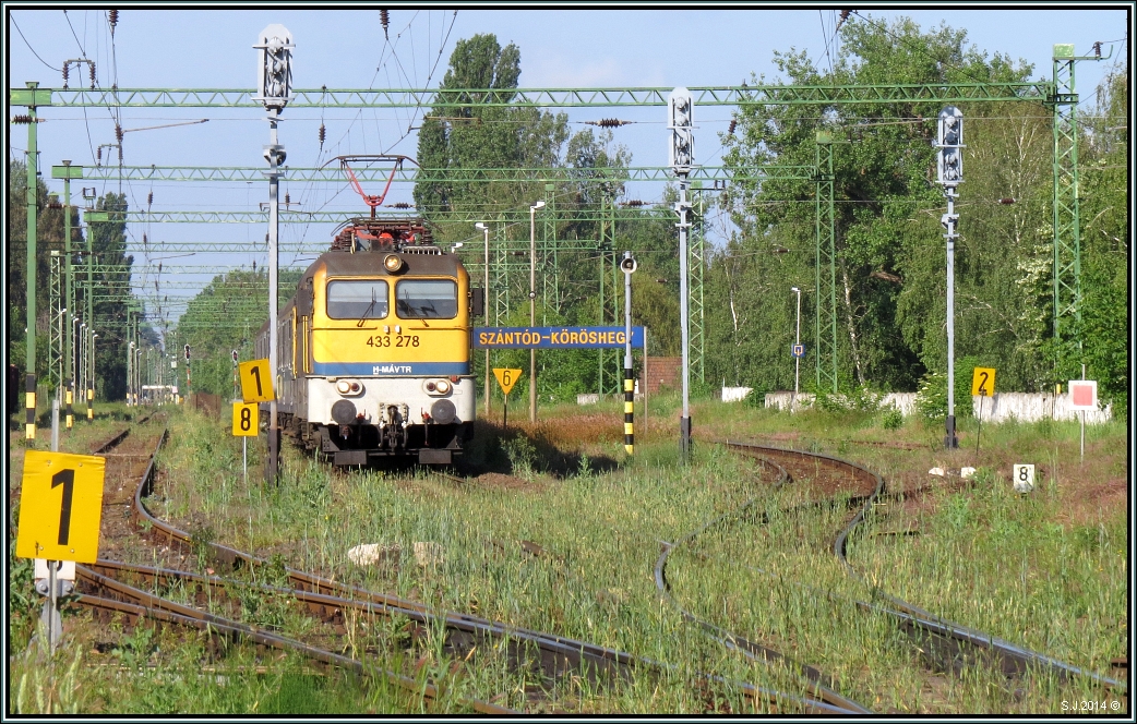 Der tiefe Einblick in den Bahnhof von Szántód - Köröshegy ,unweit vom Balatonufer.
(Vom Bahnübergang aus gesehen).Die V 433 238 mit einen Regionalexpress wartet auf die Ausfahrt nach Zamardi.Szenario vom 26.Mai 2014.