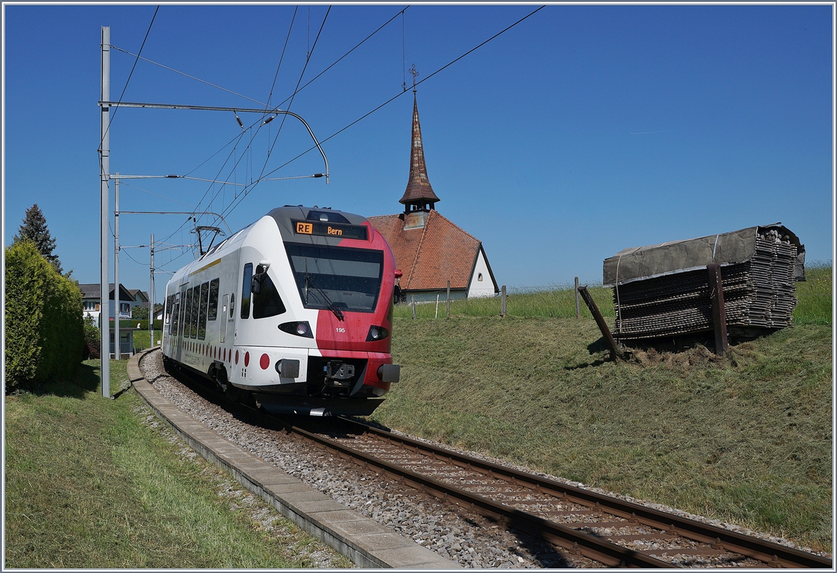 Der TPF RABe 527 195 ist bei Vaulruz auf dem Weg nach Bern, rechts im Bild , die hier typischen an den Gleisböschung stehenden Bretterstapel. 

19. Mai 2020