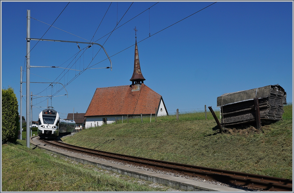 Der TPF RABe 527 198  BCF / FKB  (Kantonalbankwerbezug) erreicht Vaulruz, links im Bild die mittlerweile bekannte Kapelle von Vaulruz, rechts, die hier typischen an den Gleisböschung stehenden Bretterstapel. 

19. Mai 2020
