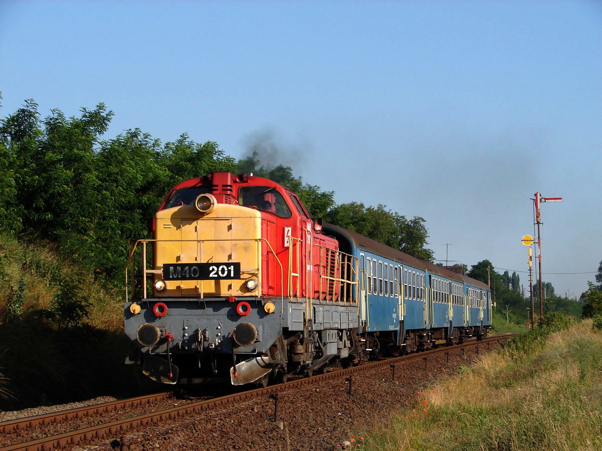 Der Turnuszug Győr - Siófok fuhr einige Jahre von 2008. Die M40 201  Bucklige) war die Zuglok im Jahr 2008. Das Bild zeigt den Zug kurz nach Kisbér. Im Hintergrund ist der Einfahrtsignal von Kisbér.
29.06.2008. 