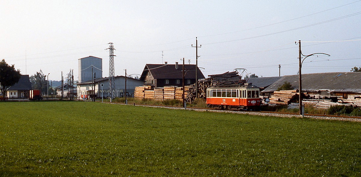 Der Tw 26.107 (ex Rheinbahn 118) hat an einem Sommerabend 1987 den links im Hintergrund sichtbaren Bahnhof St. Georgen im Attergau verlassen und fährt weiter in Richtung Attersee