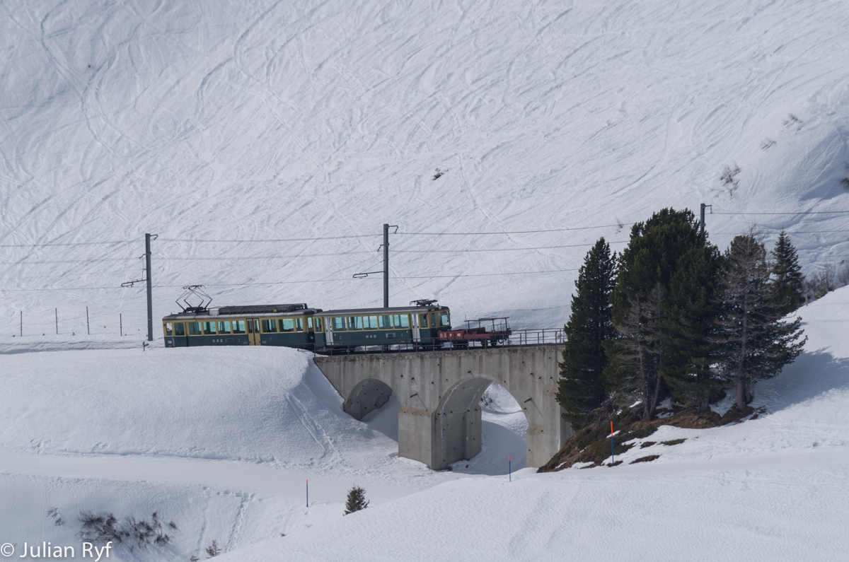 Der WAB BDhe 4/4 befindet sich mit seinem Skiverstärkungszug am 15. März 2015 unterhalb der Kleinen Scheidegg.
Gut zu erkennen ist, dass der Zug talwärts fährt - bei der Bergfahrt wäre er voll mit Skifahrern.
Hauptsächlich an Wochenenden im Winter kommen die BDhe 4/4-Pendel heute noch zum Einsatz, dann werden die planmässigen Halbstundentakt-Züge jeweils doppelt oder dreifach geführt um für die Skifahrer genug Kapazität bieten zu können. Die Züge folgen sich jeweils im Abstand von wenigen Hundert Metern. Die Kreuzungsstellen unterwegs sind lang genug für Dreifachkreuzungen.