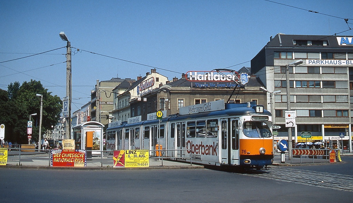 Der zehnachsige Tw 76 der ESG Linz verlässt im Sommer 1991 die Haltestelle am Blumauer Platz, ganz links ist noch das Haltestellenschild der Linie 3 zum Hauptbahnhof zu erkennen. Nachdem die Straßenbahn 2004 in einen Tunnel verlegt wurde, ist der Platz überbaut worden. Die Geoposition konnte nur anhand der beiden im Hintergrund sichtbaren Gebäude ermittelt werden.