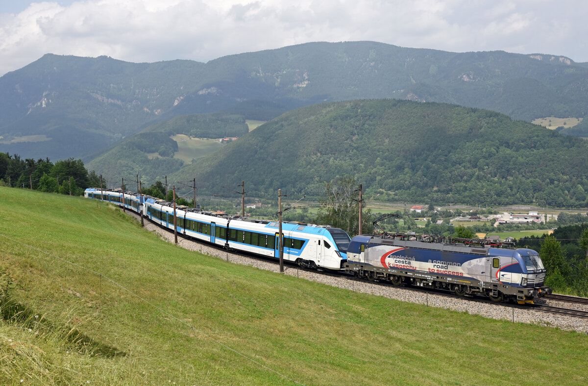 Der ZSSK-Vectron 383 204 war am 24. Juni 2021 als CDC SGAG 49483 von Breclav nach Spielfeld-Straß unterwegs. Im Schlepp befanden sich die beiden neuen SZ-FLirt 510 021 und 510 001, das Bild entstand kurz vor dem Bahnhof Eichberg auf der sogenannten Apfelwiese.