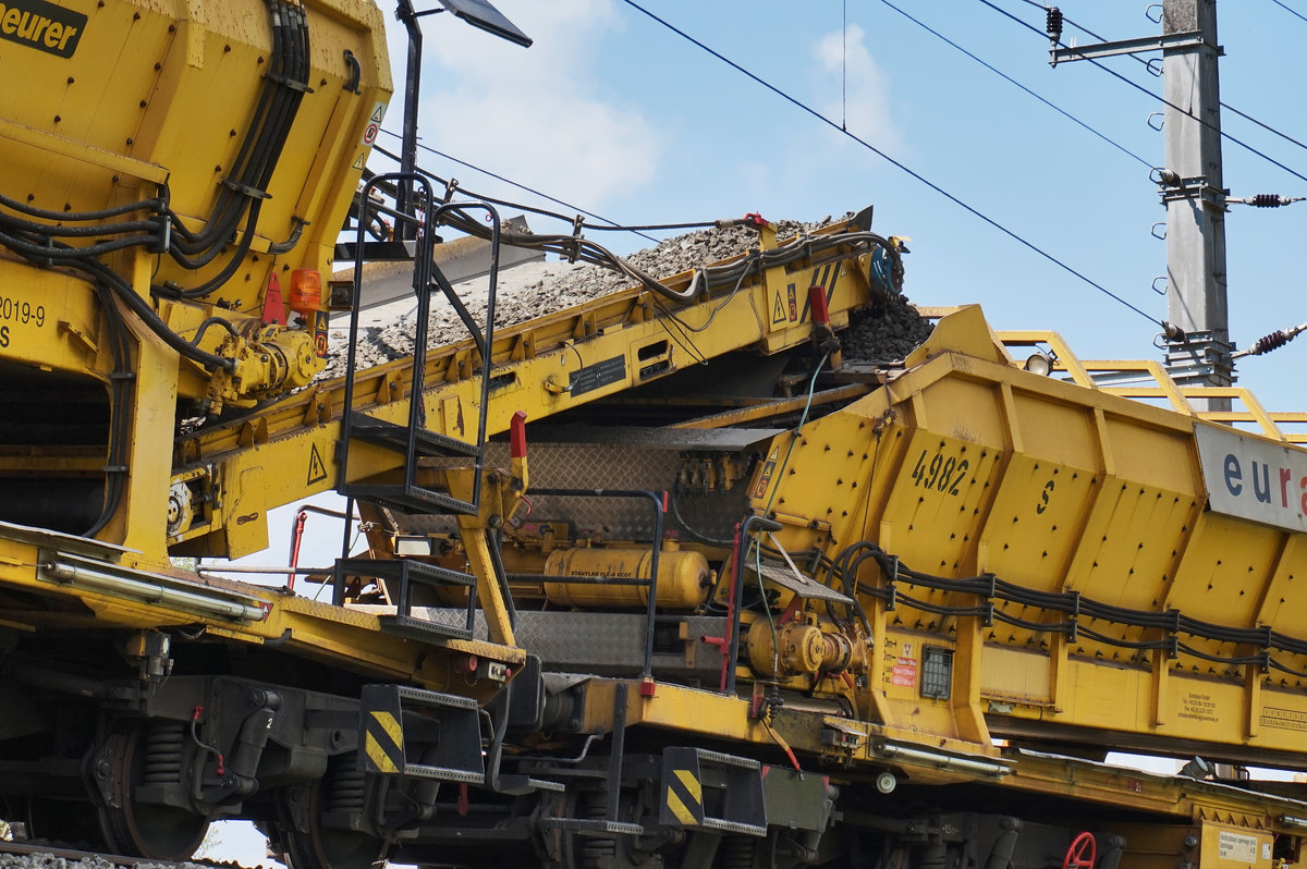 Detailaufnahme vom RU 800 S, während den Arbeiten bei Berg im Drautal:
Jeder der Schotterwagen verfügt über ein Förderband, welches den Schotter zum nächsten Schotterwagen weiter transportiert. Die Förderbänder können auch zum Entladen geschwenkt werden.
Aufgenommen am 12.4.2016
