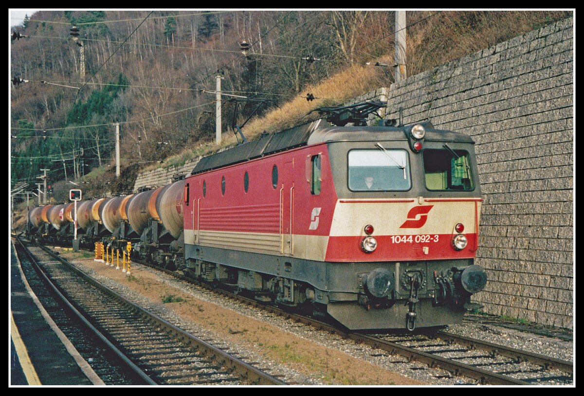 Die 1044 092 wurde nach einer Unfallausbesserung in der HW Linz im Jahr 1989 mit der Schachbrettlackierung versehen. Damit wurde sie damals ein begehrtes Fotoobjekt. Am 18.12.2000 fährt die Lok mit einem Güterzug durch Bruck an der Mur. Übrigens : Die Lok , jetzt als 1144 hat ihre Sonderlackierung  bis heute behalten.