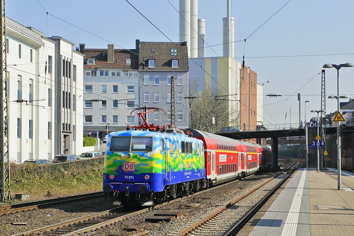 Die 111 074 wurde von DB-Gebrauchtzug im Stil der früheren Urlaubs-Express-Züge lackiert. Geplant war ein dreiwöchiger Einsatz mit dem RB 48-Ersatzzug. Am 24.03.2022 schiebt sie den Zug aus Wuppertal-Barmen nach Oberbarmen.