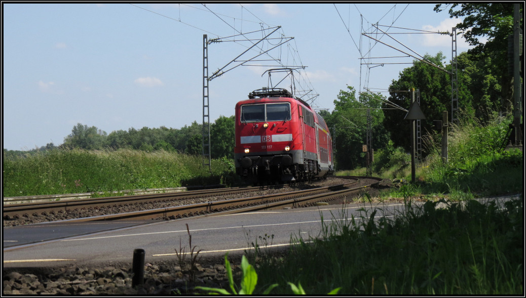 Die 111 117 zieht den Wupper Express (RE4) in Richtung Aachen. Hier zu sehen aus der Froschperspektive am Bahnübergang bei Rimburg,unweit von Übach Palenberg auf der Kbs 485 am 10.Juni 2015.