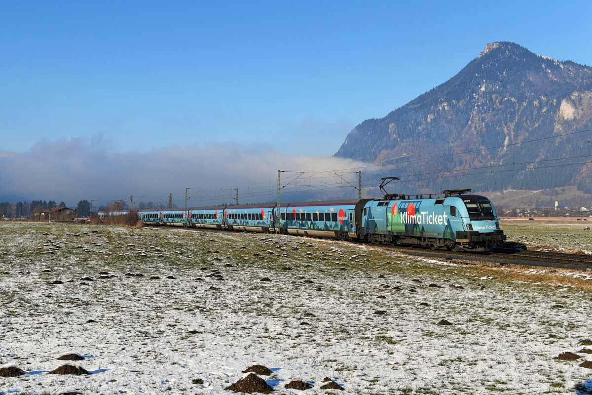 Die 1116.244 macht samt kompletter Wagengarnitur auf das österreichische Klimaticket aufmerksam. Am 15. Januar 2022 kam der sogenannte  Klimajet  als RJ 860 von Wien HBF nach Bregenz zum Einsatz. Bei Niederaudorf konnte ich den bunt gestalteten Zug aufnehmen. Im Hintergrund erkennt man die bereits auf Tiroler Gebiet liegende Ortschaft Erl und das imposante Kranzhorn.  