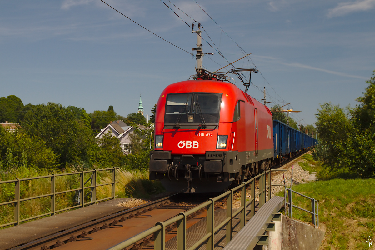 Die 1116.272 passiert auf ihrer Fahrt Richtung Absdorf-Hippersdorf gerade die Brücke über den Göllersbach in Stockau. Links neben der Lokomotive der Kirchturm von St.Stephan. (10.07.2020)