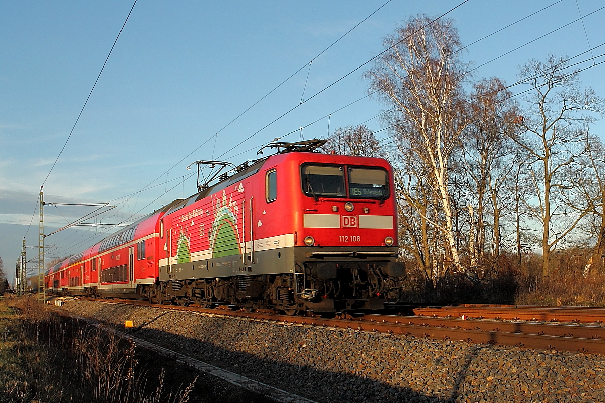Die 112 108 –Genau Ihre Richtung- mit dem RE 4361 auf der RE 5 von Rostock Hbf nach Elsterwerda am 19.12.2015 in Nassenheide.
Mit dem Fahrplanwechsel wurden die südlichen Zielorte verändert, vorher war die Linie Rostock-Lutherstadt Wittenberg.
