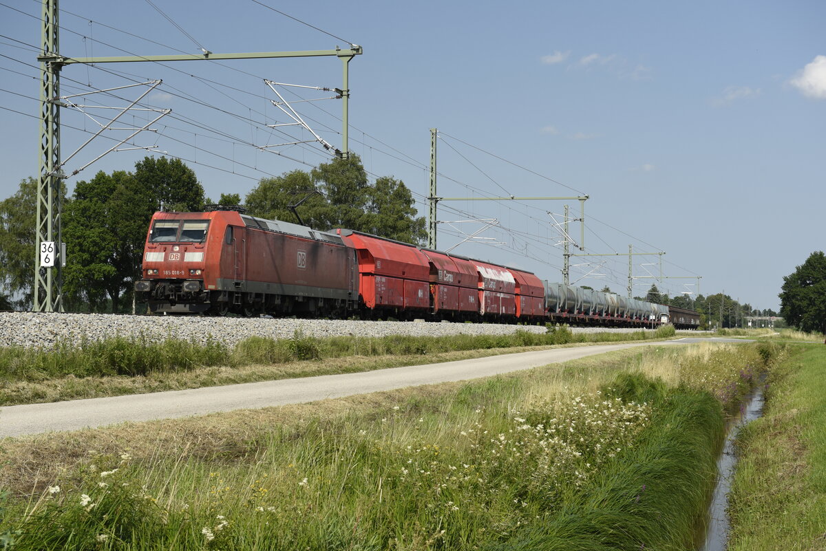 Die 185 018-9 der DB mit einem gemischten Güterzug auf der Strecke in Richtung München kurz nach Übersee am Chiemsee. Aufgenommen am 23.07.21 