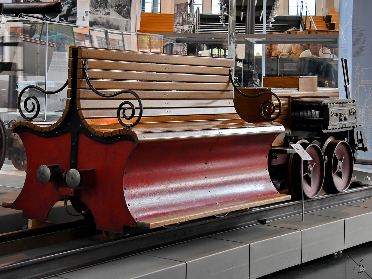 Die 1879 von Siemens gebaute Elektrolokomotive besteht aus einem einfachen Fahrgestell mit einem ummantelten Gleichstrommotor. (Verkehrszentrum des Deutsches Museums München, August 2020) [Genehmigung liegt vor]