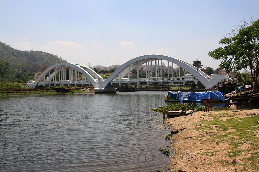 Die 1919 fertiggestellte 87,3m lange Tha Chomphu Bridge über den Mae Nam Tha, von den Einheimischen Saphan Khao (=Weiße Brücke) genannt, gilt als eines der Wahrzeichen der Provinz Lamphun und ist deshalb ein Touristen-Hotspot mit Parkplatz, Informationsstand, Parkanlage und sogar mit einer Treppe auf den Bahndamm. Bild vom 22.März 2023.