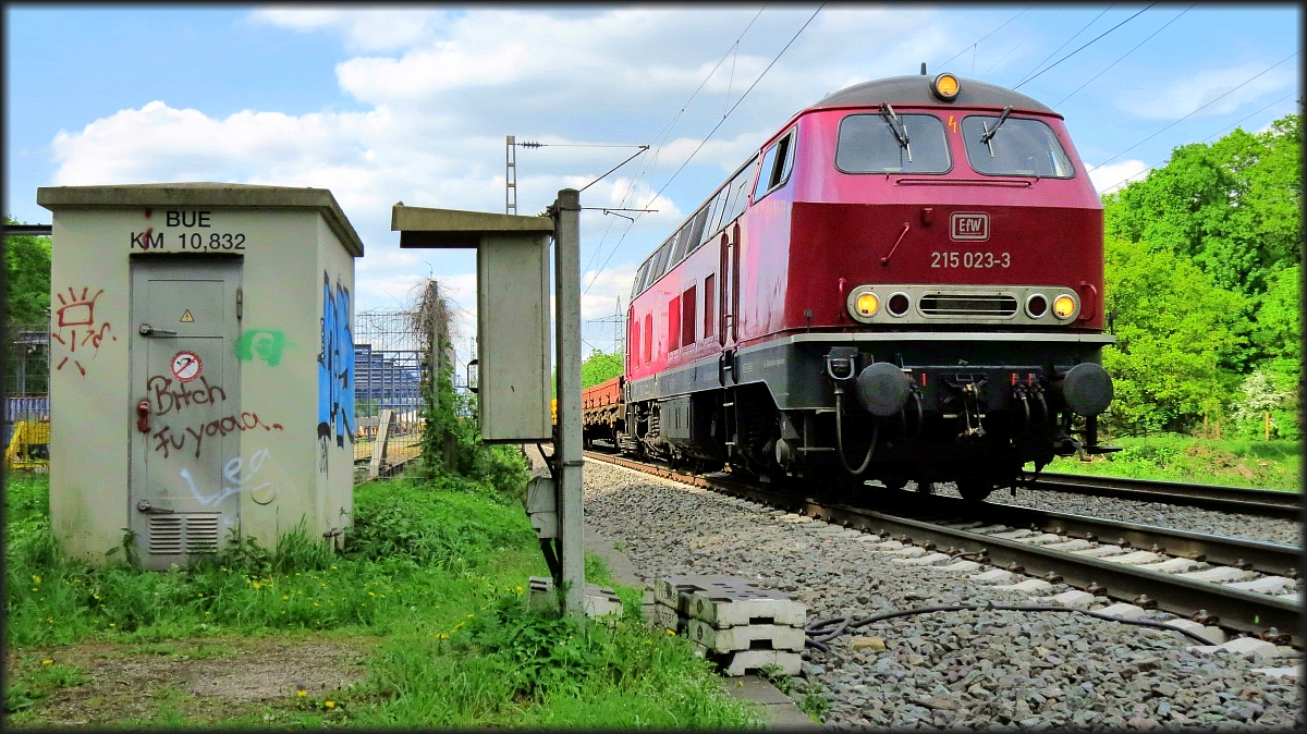 Die 215 023-3 der EfW ist mit einen leeren Flachwagenzug am Haken in Richtung Düsseldorf unterwegs. Hier zu sehen am BÜ unweit vom Voest Alpine Schienenlager bei DU Wedau. Datiert vom 03.Mai 2018.