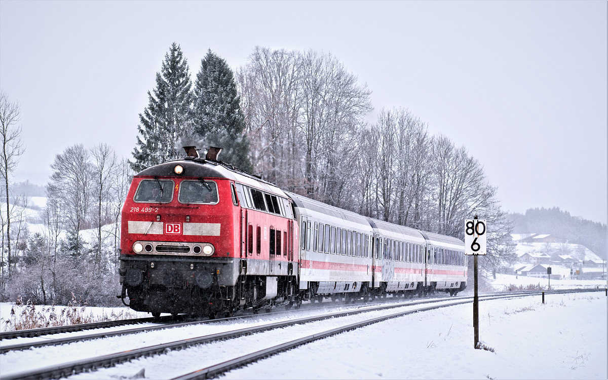 Die 218 499-2 fährt in Stein im Allgäu bei leichtem Schneetreiben mit dem IC 2085 Nebelhorn nach Oberstdorf vorüber.Bild 12.12.2017