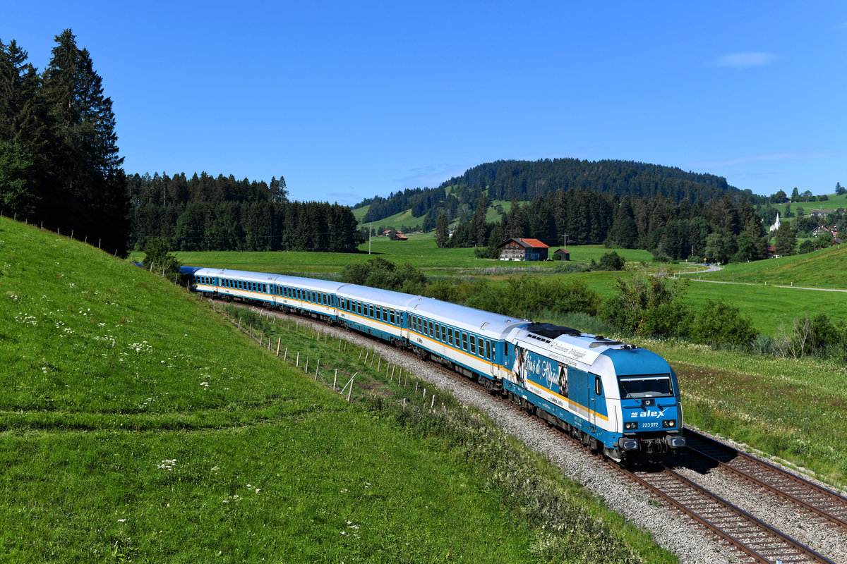 Die 223 072 trug auch im Jahr 2020 noch eine Seitenwerbung, welche auf das „Gautrachtenfest D’Wageggler“ hinweisen sollte. Mit einem Trachtenpaar und der Aufschrift  Griaß di, Allgäu!  möchte man die Verbundenheit zur Region unterstreichen. Am 05. Juli 2020 konnte ich die Lok mit ihrem ALX 84104 auf der Fahrt nach Hergatz bei Weißenbachmühle aufnehmen.