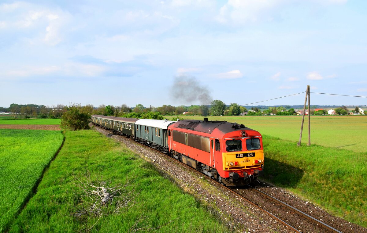 Die 418 128 (M41 2128) ist nach Veszprémvarsány mit dem Zug 39526. Hinter der Lokomotive fährt ein 105 Jahre alter Speisewagen. 
Veszprémvarsány, 07.05.2023.
