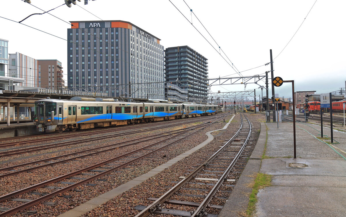 Die Ainokaze Toyama Bahn, eine der drei neu entstandenen Privatbahnen im Hokuriku-Gebiet: Zwei Zweiwagenzüge bei der Einfahrt in den Bahnhof Takaoka. Vorne Zug 521-18 (ehemals JR), dahinter der neu beschaffte Zug 521-1002. Beide Züge zeigen sich hier von der  blauen Seite , die andere Seite ist grün. 20. März 2024 