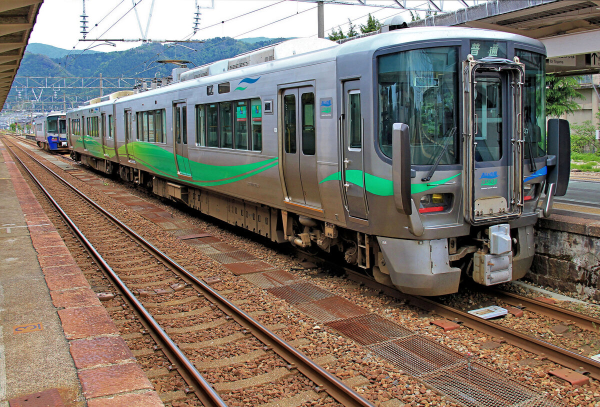 Die Ainokaze Toyama Bahn fährt vollständig unter Wechselstrom; es werden jedoch Zweistrom-Züge (Wechselstrom 20 kV/60 Hz / Gleichstrom) benützt, um auf angrenzende JR-Gleichstromstrecken einfahren zu können. Der Bahn gehören 100, 1 km Strecke quer durch die Praefektur Toyama, von der Grenze zur IR Ishikawa-Bahn im Westen im Dorf Kurikara durch die Städte Takaoka und Toyama hindurch nach Ichiburi im Nordosten; die elektrischen Züge enden allerdings kurz vorher in Tomari (90, 7 km von Kurikara), und die Fahrgäste müssen auf den nördlich anschliessenden Dieseltriebwagen der Echigo Tokimeki Bahn umsteigen. Im Bild der Ainokaze Toyama Bahn Zweiwagenzug 521 Nr.18 auf seiner grünen Seite (die andere Seite ist blau) an der Endstation Tomari im Nordosten der Praefektur Toyama. Dahinter wartet der Dieseltriebwagen ET 122-6 der Echigo Tokimeki Bahn auf die wenigen Passagiere, die auf der nun zur Lokalbahn gewordenen Strecke weiter Richtung Norden fahren wollen. 13. Mai 2016 