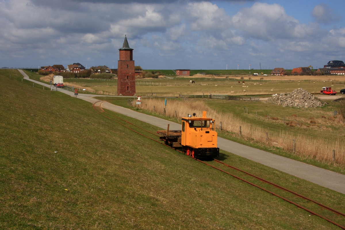 Die Auffahrt zur Deichkrone kommt Lok 1 (Schöma 4816, Bj. 1985) mit einem Plattenwagen herauf, im Hintergrund , am alten Unterfeuer Dagebüll, die Zufahrt zum Bh. (23.04.2010)