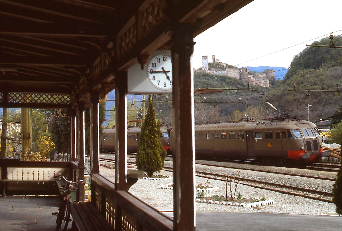 Die Bahnhofsuhr zeigt 16.45 Uhr, als eine ALe 840-Doppeltraktion im März 1985 in  Siegmundskron/Ponte d'Adige einfährt. Im gleichnamigen Schloss im Hintergrund befindet sich heute eines der sechs Mountain Museen des Südtiroler Bergsteigers Reinhold Messner.